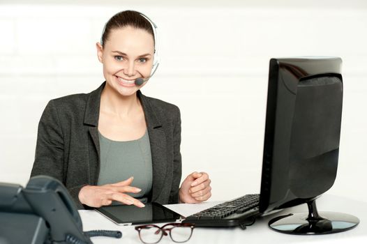 Customer care executive using tablet pc wearing headsets and looking at camera