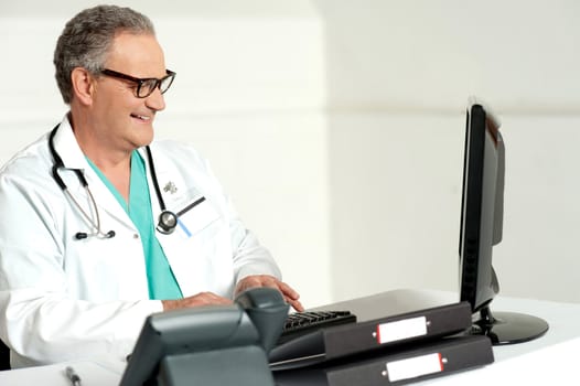 Experienced smiling male doctor working on computer, typing on keyboard