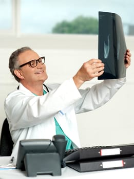 Aged surgeon holding patients x-ray report and reviewing it. Sitting in his clinic