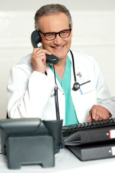 Matured physician communicating on phone sitting on chair in his lab