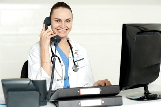 Young smiling physician sitting in clinic and communicating on phone