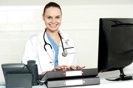 Cheerful female doctor tying on keyboard looking at you