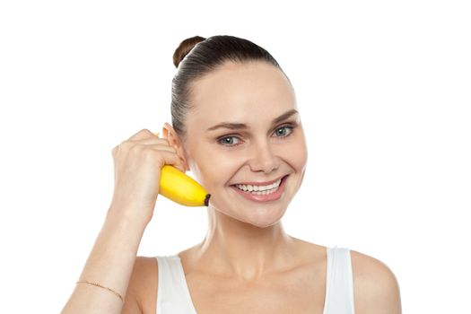 Girl doing call gesture using banana as cellphone. All on white background