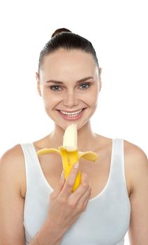 Cheerful fit woman eating banana and smiling at camera