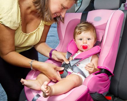 Woman fastening her son on a baby seat in a car 