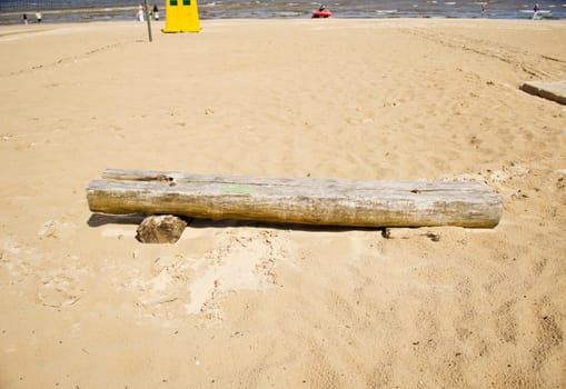 Old broken wooden bench in sea sand. People relax near sea. Yellow garbage box.