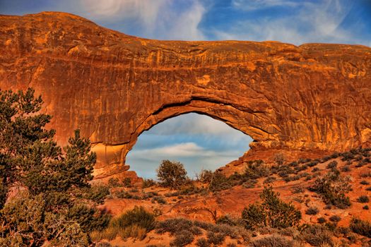 The rays of the setting sun add a golden glow to massive natural stone archway in Utah.