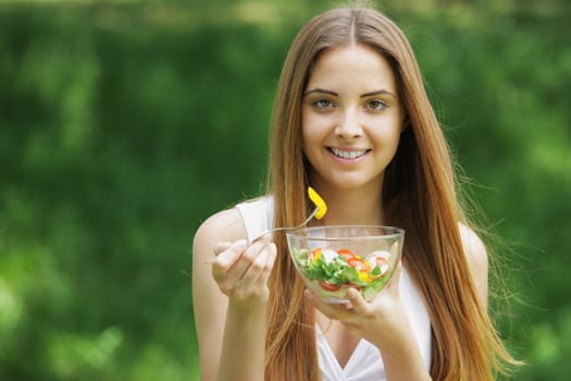 Close-up of happy beautiful young woman eating vegetable salad