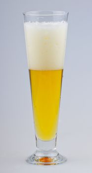 A glass of beer with foam over gray background