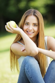 Young smiling woman outdoors holding an apple