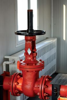 Red metal regulator valve with a top mounted wheel to rotate to control water flow for firefighting