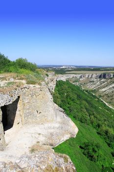 Summer landscape with cave in rock on blue sky background