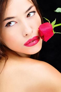 Pretty woman and red rose near lips on black background