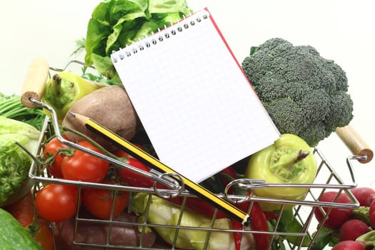 Basket with fresh vegetables, shopping list and pencil