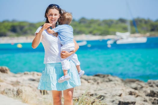 Young beautiful woman wis her son walking along tropical beach