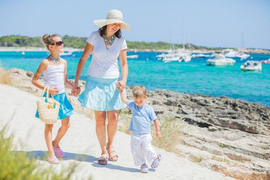 Young beautiful family of three walking along tropical beach