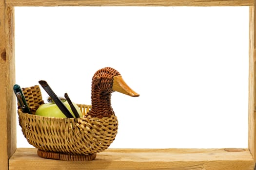 Wicker basket with a ball-point pens and brushes  and green apple in a wooden frame on white background