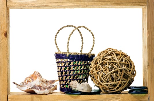 Wicker, green pieces of glass and sea shells inside rough wooden frame on white background