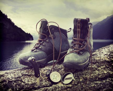 Hiking boots with compass on tree trunk near lake