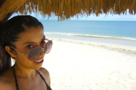 Young latin woman standing under a Palapa with beach in the background