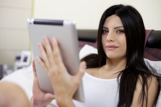 Closeup of gorgeous elegant woman in bed with tablet connecting to internet smiling