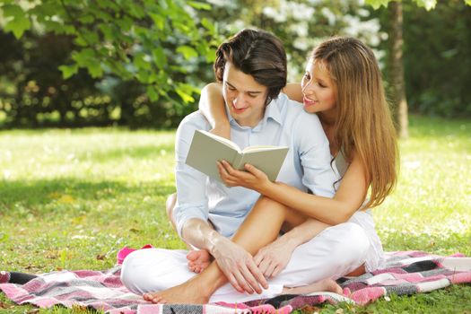 a young couple read a book together in the park