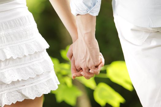 a couple of young lovers strolling holding hands in a park, close up of the hands