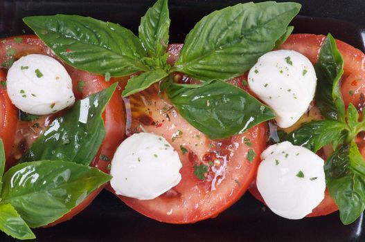 Italian Caprese Salad with Basil, Fresh Mozzarella, Tomatoes and Olive Oil on black plate close up