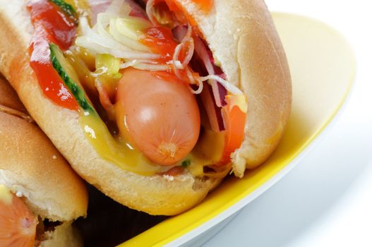 Hot Dog with Sausage, Vegetables, Ketchup and Mustard close up on yellow plate