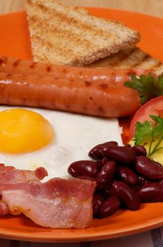 English Breakfast with Sausage, Bacon, Fried Eggs Sunny Side up, Beans, Tomato and Toasts close up on orange plate