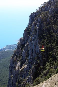 Yellow overhead cable car on background with very high mountain and sea