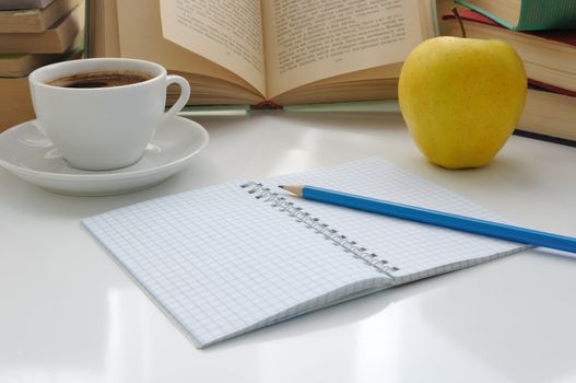 Notebook with a pencil on a table with a cup of coffee and an apple on the background of the books