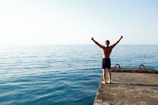 Teenage boy standing on pier against sea with hands up