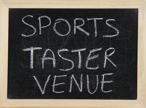 A blackboard with a wooden border with the words 'SPORTS TASTER VENUE' written by hand in white chalk.