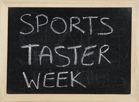 A blackboard with a wooden border with the words 'SPORTS TASTER WEEK' written by hand in white chalk.