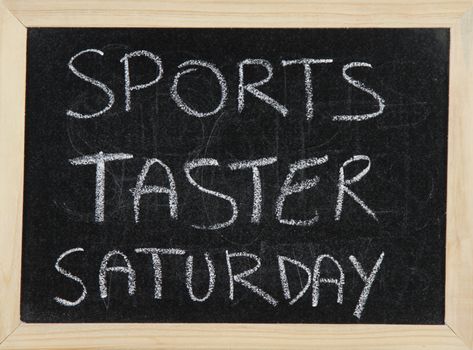 A blackboard with a wooden border with the words 'SPORTS TASTER SATURDAY' written by hand in white chalk.