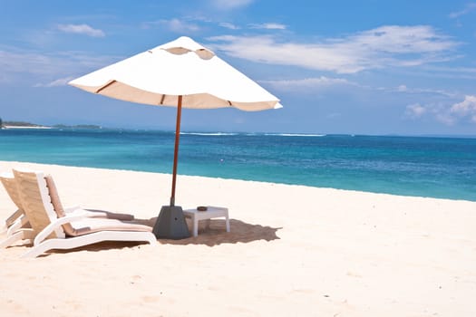 Idyllic beach scene, white sand and the blue sea and an umbrella with chairs