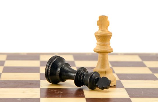 Black chess king lie near winner white on chess board isolated on white.