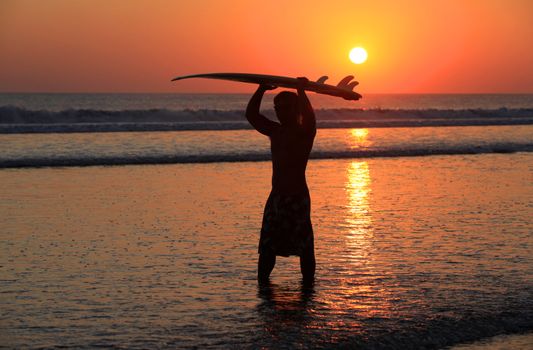 Silhouettes of surfer at red sunset. Kuta beach. Bali