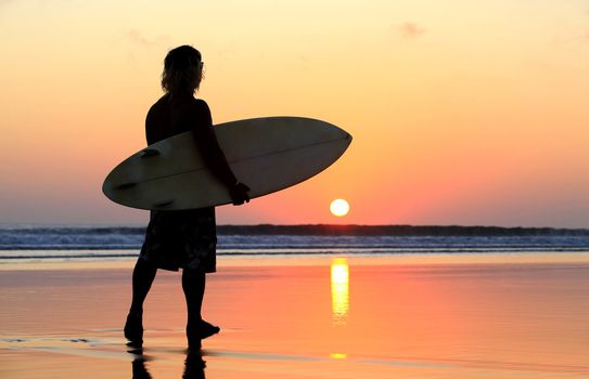 Silhouette of surfer at red sunset. Kuta beach. Bali