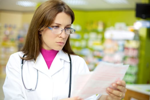 Serious woman doctor in pharmacy reading with glasses medical prescription