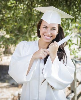 Attractive Mixed Race Girl Celebrating Graduation Outside In Cap and Gown with Diploma in Hand.