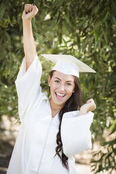 Attractive Smiling Mixed Race Girl Celebrating Graduation Outside In Cap and Gown.