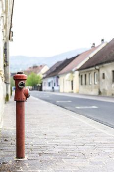 Red fire hydrant located on a sidewalk of village street.