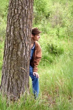 Young man hiding behind a tree