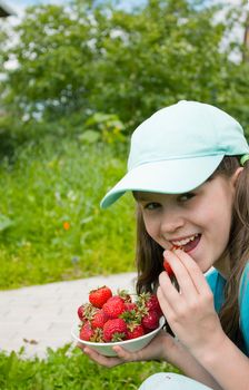 Little girl eats ripe strawberry in garden