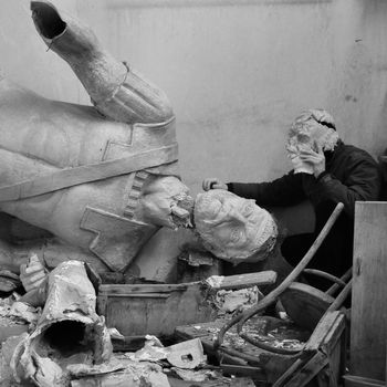 Broken statue in the vandalized studio of Greek sculptor Nikolas Pavlopoulos (1909 - 1990). Abandoned interior and masked figure, Athens Greece, 2012.