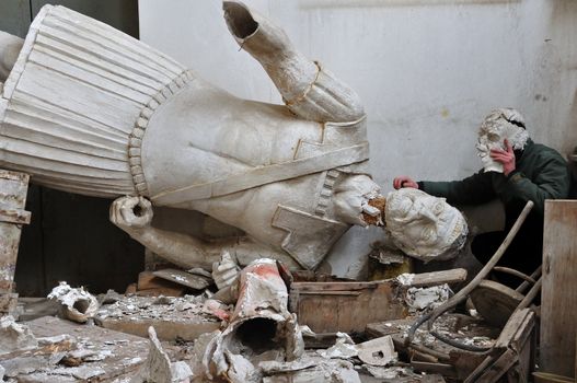 Broken plaster statue of ancient god in the vandalized studio of Greek sculptor Nikolas Pavlopoulos (1909 - 1990). Abandoned interior and masked figure, Athens Greece, 2012.