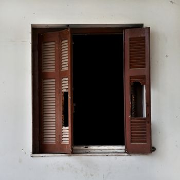 Wooden window shutter cracked open and dirty wall of an abandoned house.
