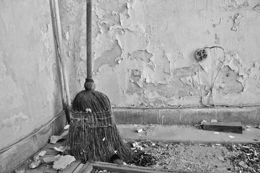 Dusty straw broom on filthy floor of abandoned house. Black and white.